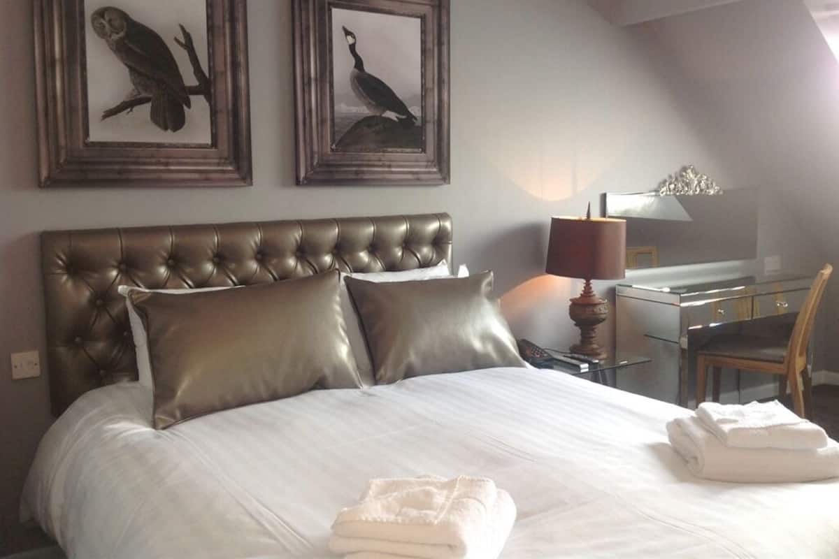 Habitación de hotel con una cama grande, dos obras de arte enmarcadas, un escritorio con lámpara y una silla.