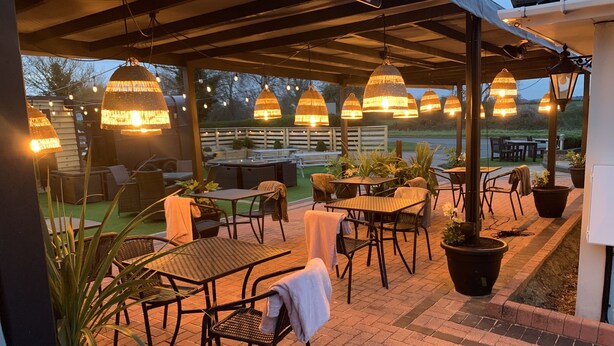 Eine Terrasse im Freien mit Tischen, Stühlen, Lichterketten und Blumentöpfen.