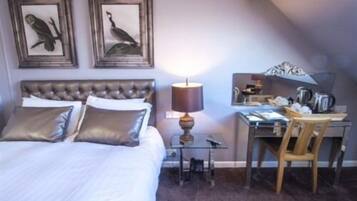 A bedroom with a large bed, a desk, and two wall-mounted bird paintings.