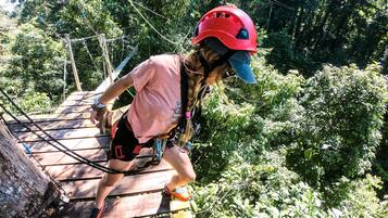 A person on a wooden bridge with safety harnesses, surrounded by dense greenery.