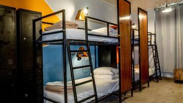 A dormitory room with bunk beds, a ladder, a desk, and a lamp.