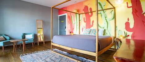 A room with a four-poster bed, a wooden floor, a blue sofa, a small table, and a colorful wall mural.