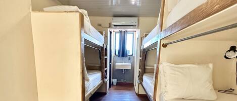 A narrow corridor with bunk beds on either side, a small stool, and a window at the end.