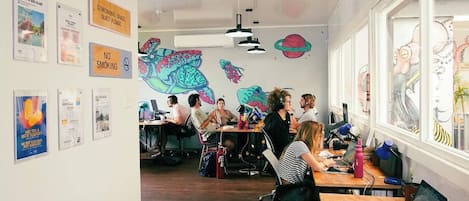 A modern co-working space with wooden desks, multiple workstations, and colorful murals on the walls.