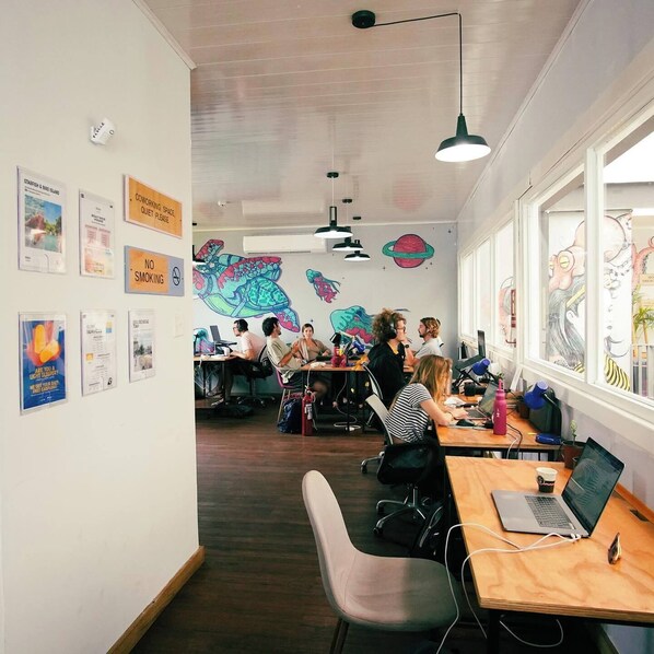 Un espacio de coworking moderno con escritorios de madera, varias estaciones de trabajo y murales coloridos en las paredes.
