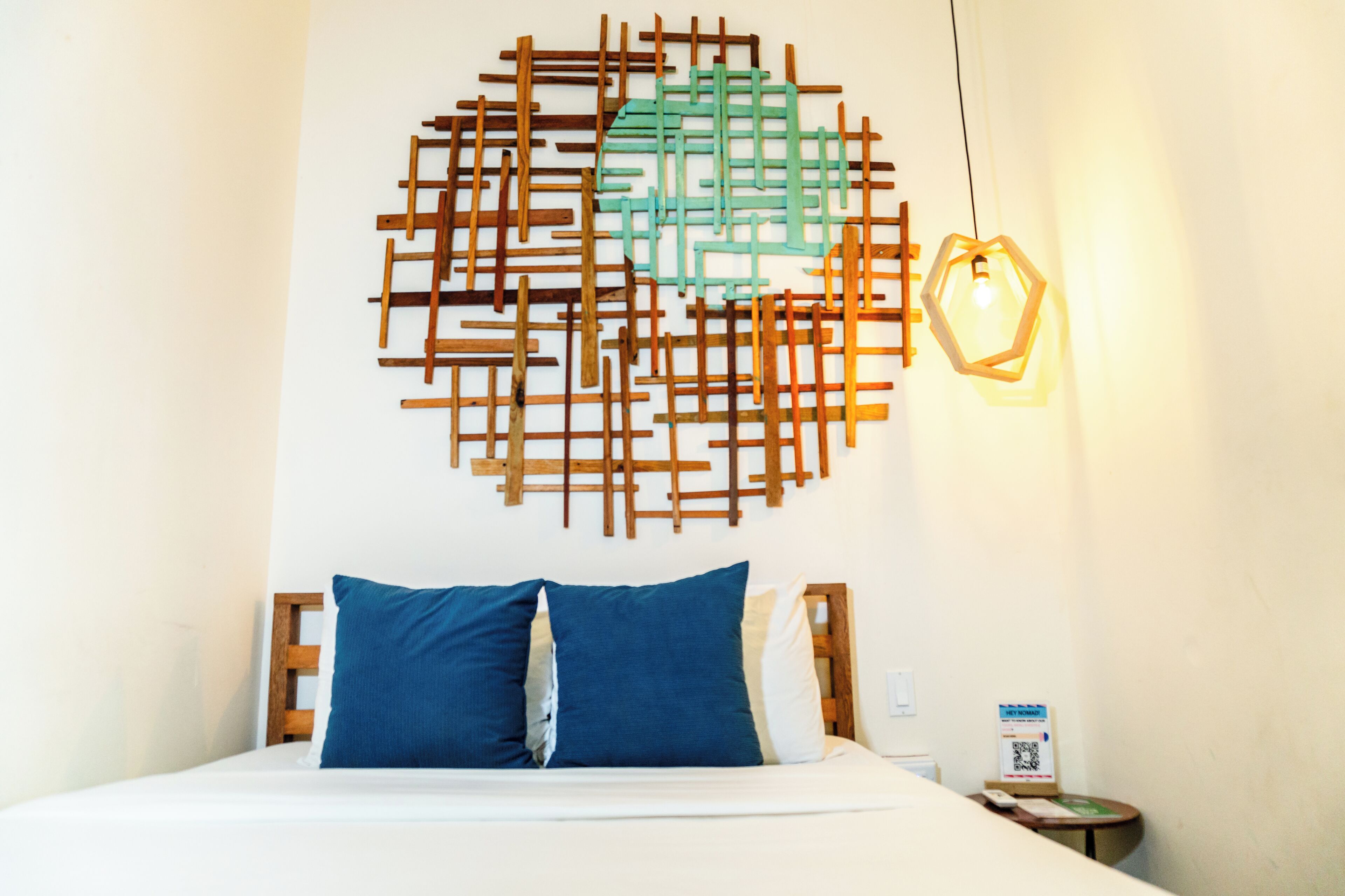 A hotel room with a bed, a wooden headboard, a wall art piece, and a hanging light fixture.