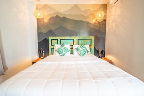 A bed with a white quilted bedspread, two green patterned pillows, and a headboard with a mountain mural.