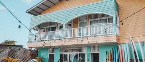 A two-story building with a balcony, surfboards, and a sign for a surf school.