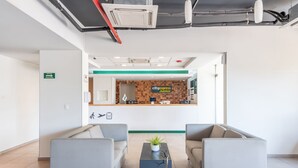 Een receptie met een balie, twee grijze banken, een bijzettafeltje met een plant, en een bordje dat een rookruimte aangeeft.