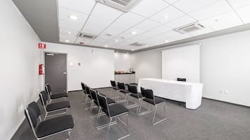 A conference room with a white table, black chairs, a projector screen, and a fire extinguisher.