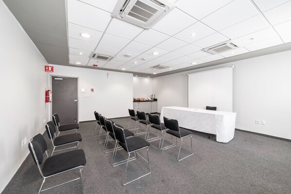 A conference room with a white table, black chairs, a projector screen, and a fire extinguisher.