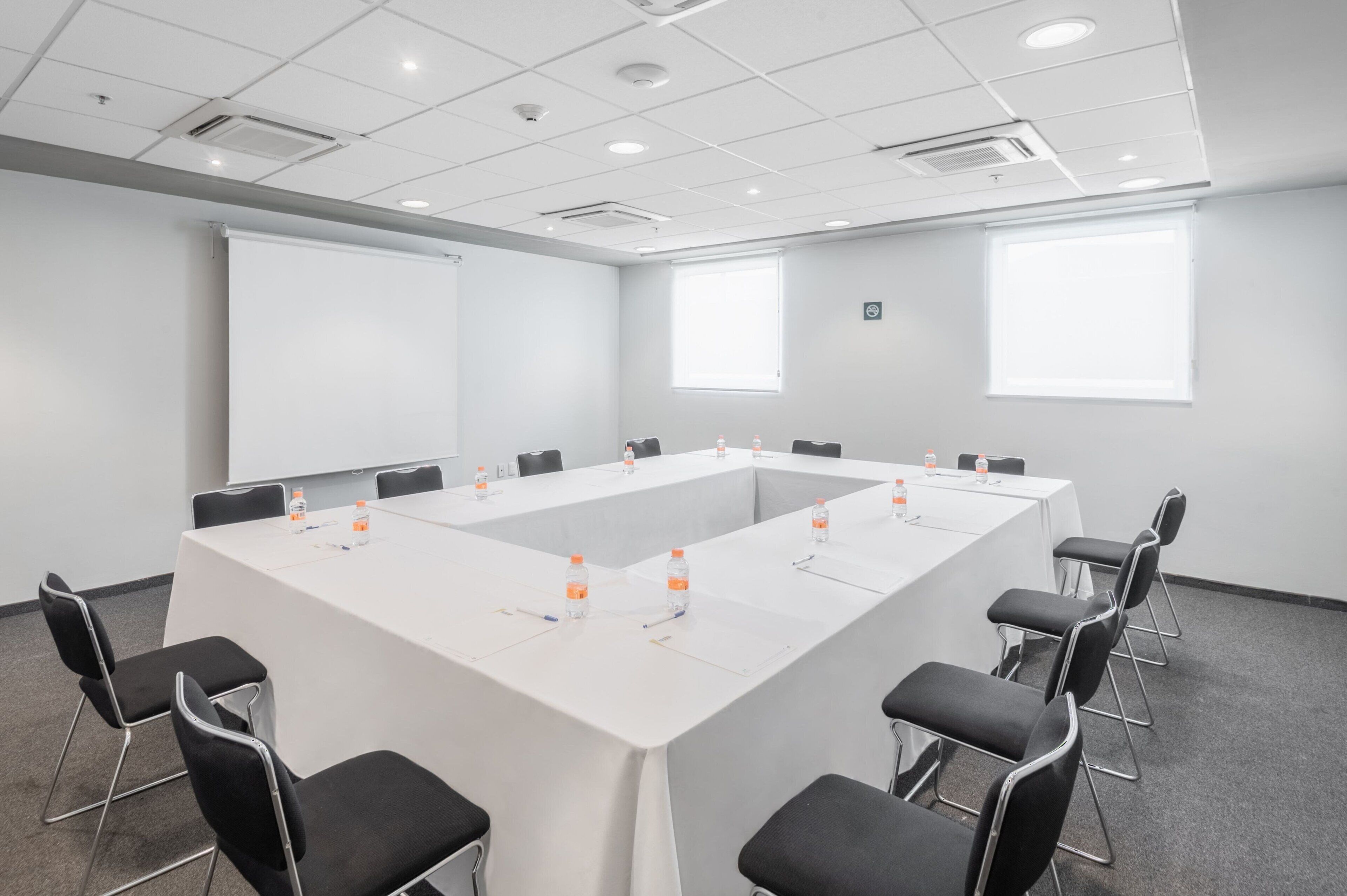 Una sala de conferencias con una larga mesa, sillas negras y una pantalla de proyector.