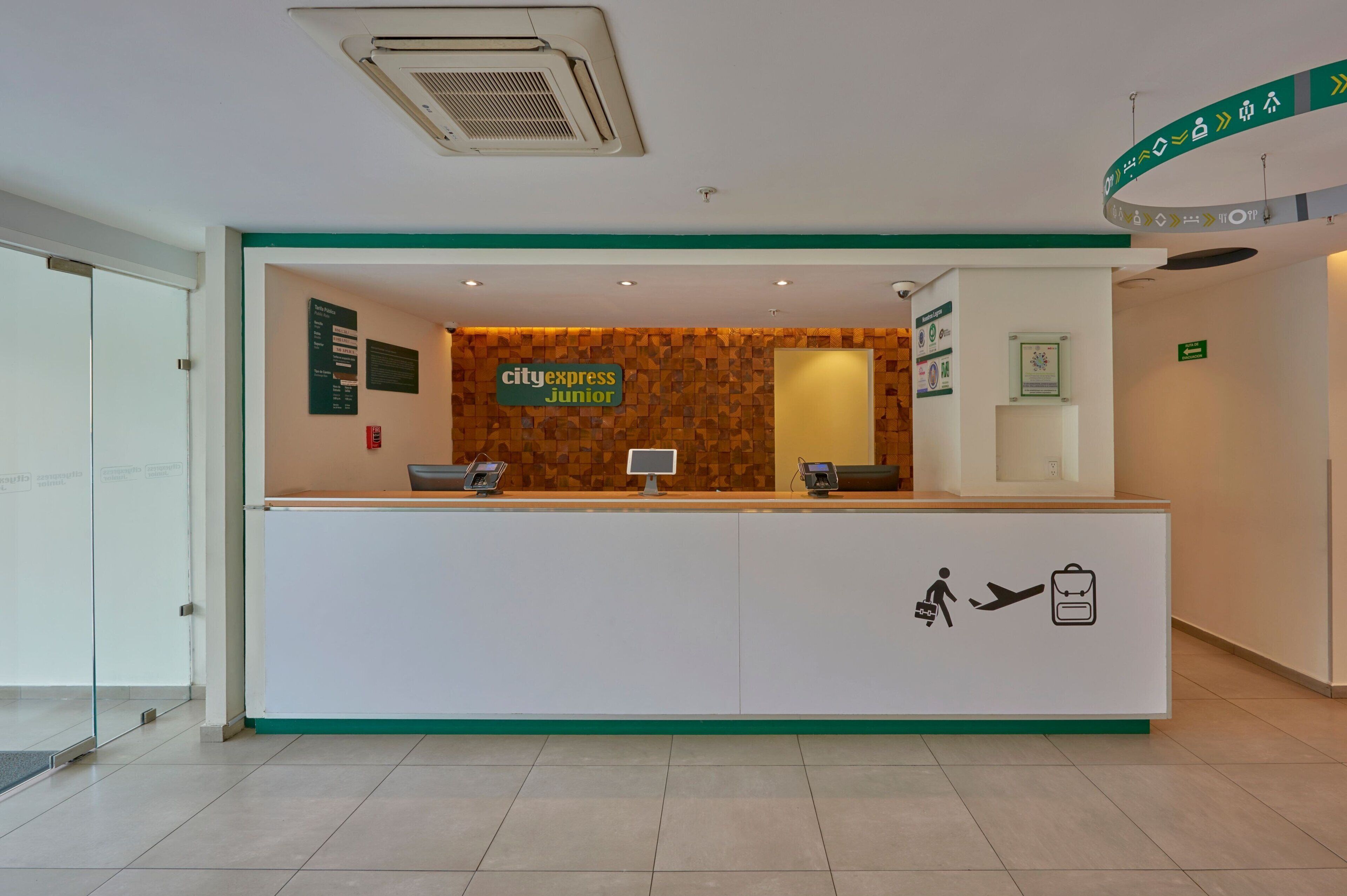 Una recepción con un cartel que dice "cityexpress junior", una pantalla digital y un letrero que indica un baño.