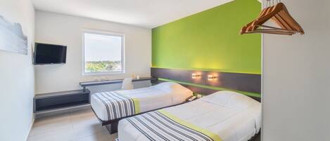 A hotel room with two beds, a TV, a window, and a green accent wall.