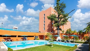 Een hotel met een zwembad, terras en een hoge bebouwing op de achtergrond.