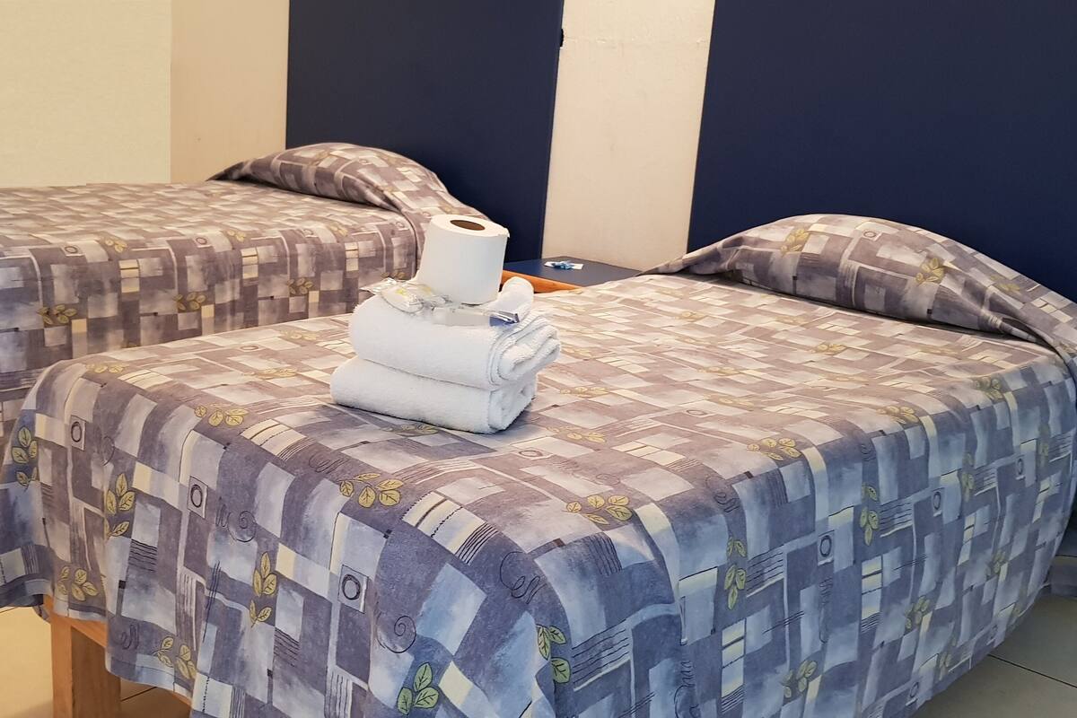 Deux lits simples avec une literie à motifs, une serviette enroulée et un rouleau de papier toilette sur la table de chevet.