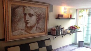A room with a checkered sofa, a painting, a coffee station, and a fruit bowl.