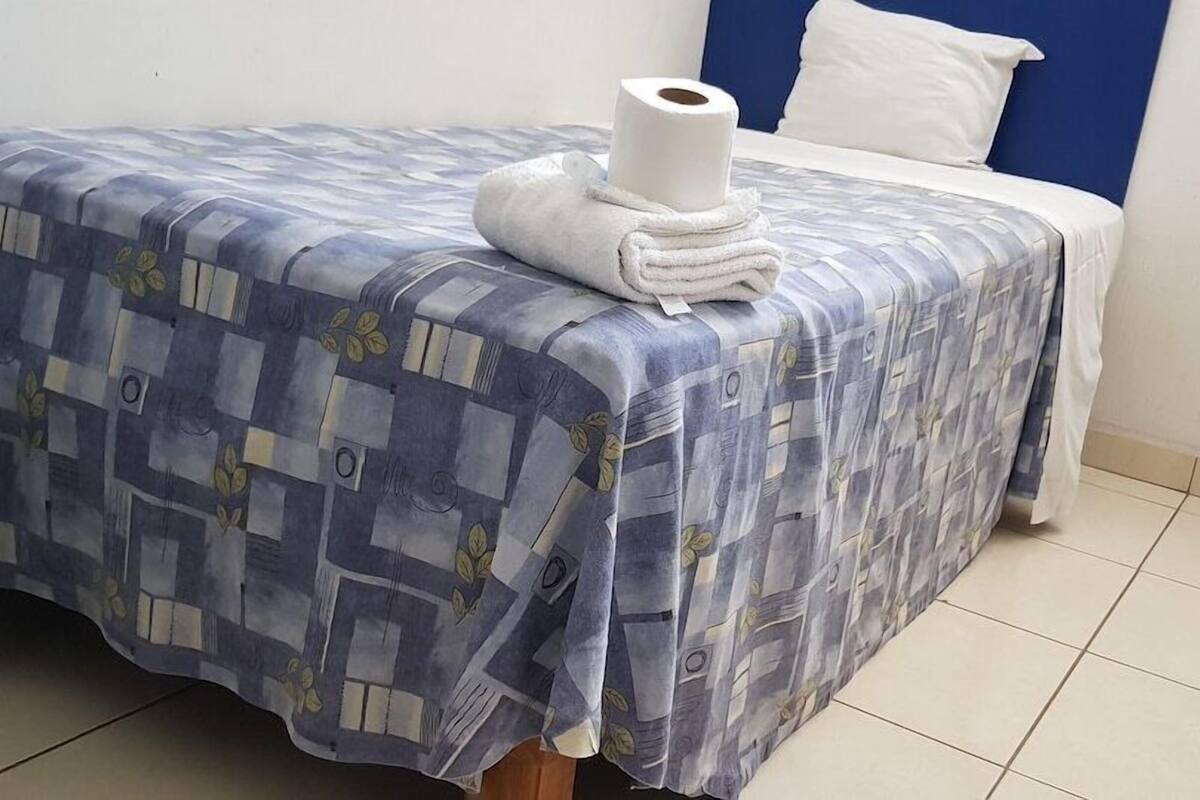 Un lit avec une couvre-lit à motifs, une serviette enroulée et un oreiller blanc.