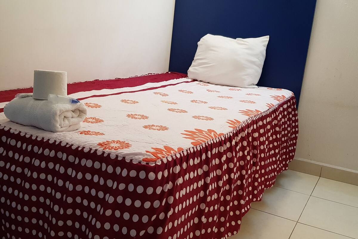 Un lit bien fait, avec une couvre-lit à pois, un oreiller blanc et une serviette enroulée posée sur le côté.
