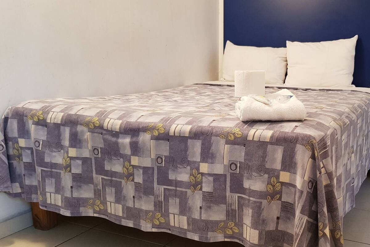 Un lit bien fait, avec une couvre-lit à motifs, une serviette pliée et une table de chevet sur laquelle se trouve une lampe.