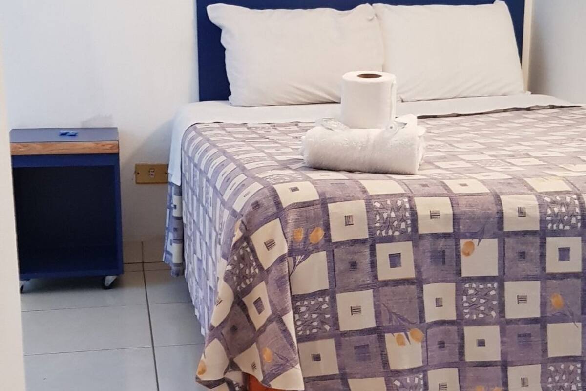 Un lit avec une couvre-lit à motifs, un oreiller blanc et une serviette enroulée sur le côté.