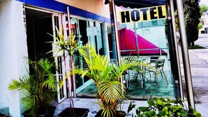 A hotel entrance with a glass door, a red awning, and outdoor seating.