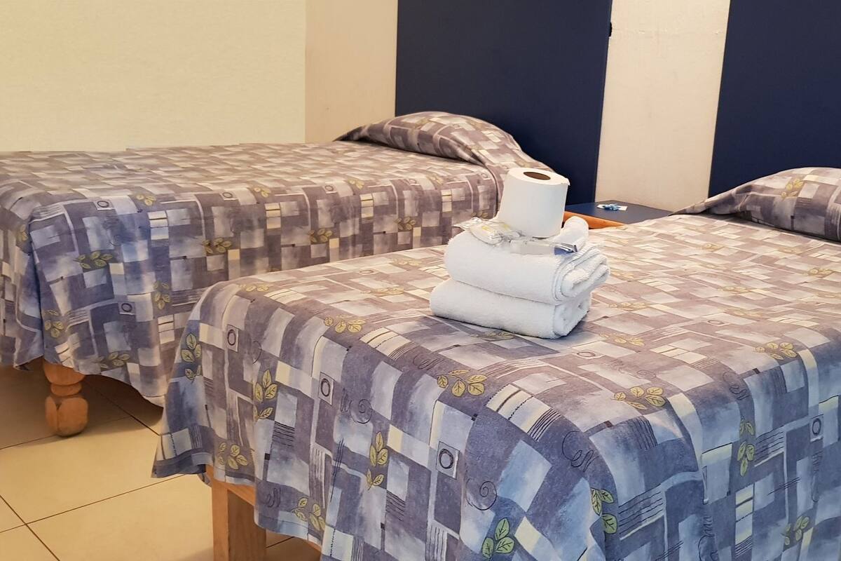 Deux lits avec une literie à motifs, une serviette enroulée et un rouleau de papier toilette sur la table de chevet.