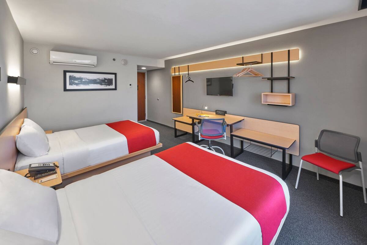 Habitación de hotel con dos camas, un escritorio, una silla, un televisor y un armario.