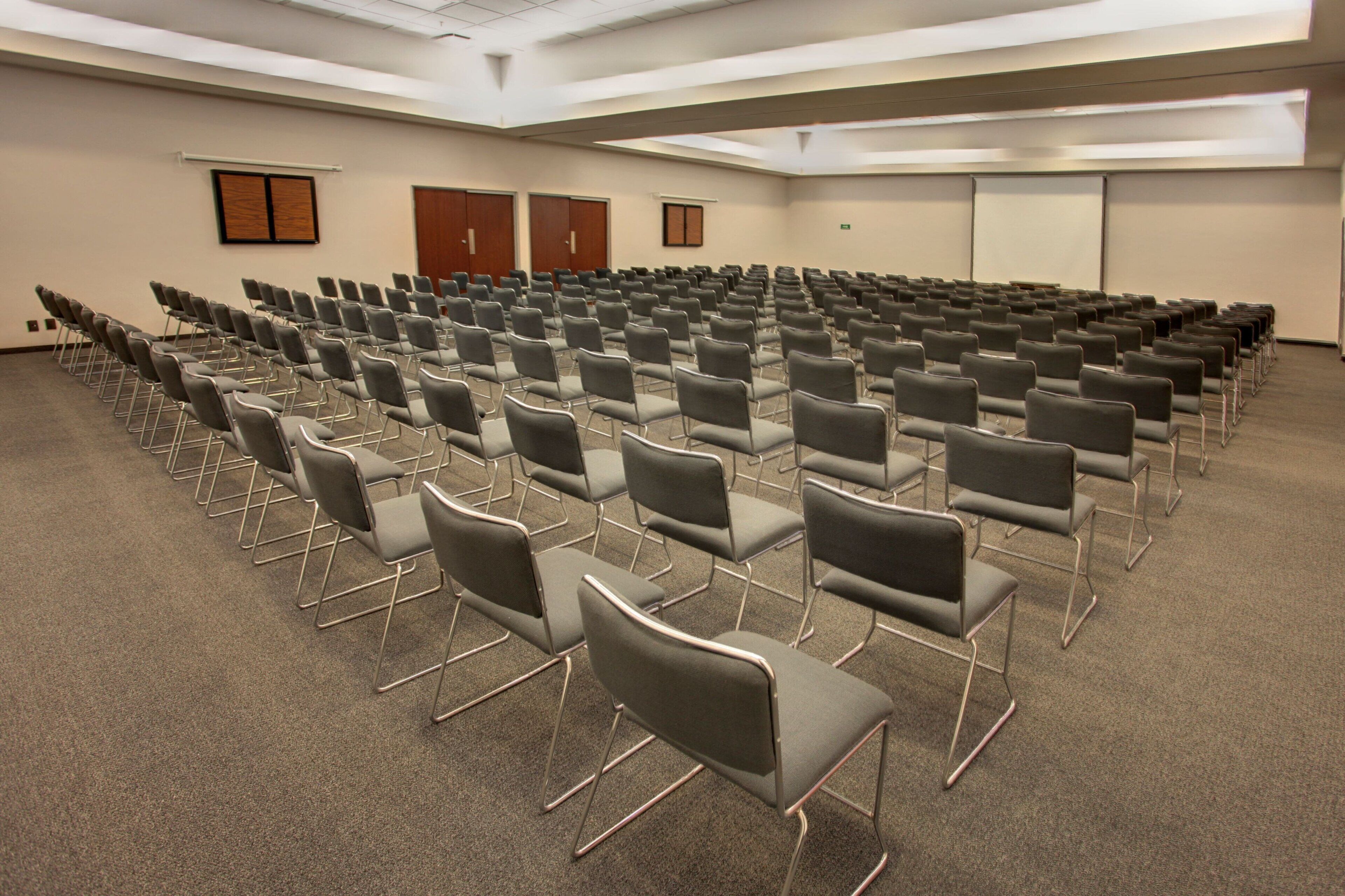 A conference room with rows of grey chairs, a carpeted floor, and a whiteboard on the wall.