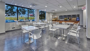A modern cafeteria with white tables and chairs, large windows, and a no smoking sign.