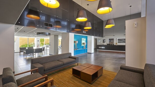 A spacious lobby with a modern design, featuring a grey sofa, wooden coffee table, and pendant lighting.