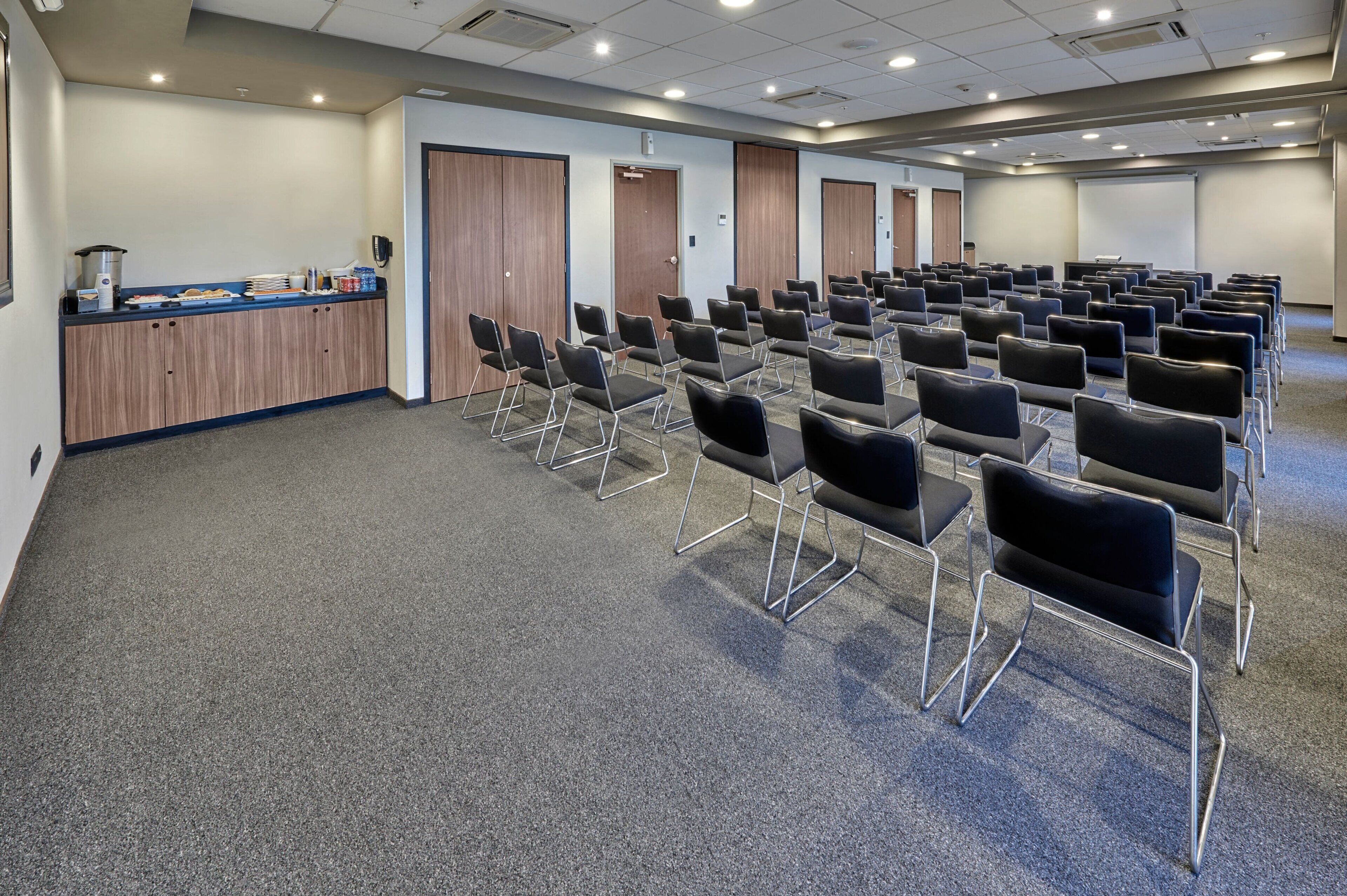 Un salón de conferencias con filas de sillas, un atril y una mesa de buffet.