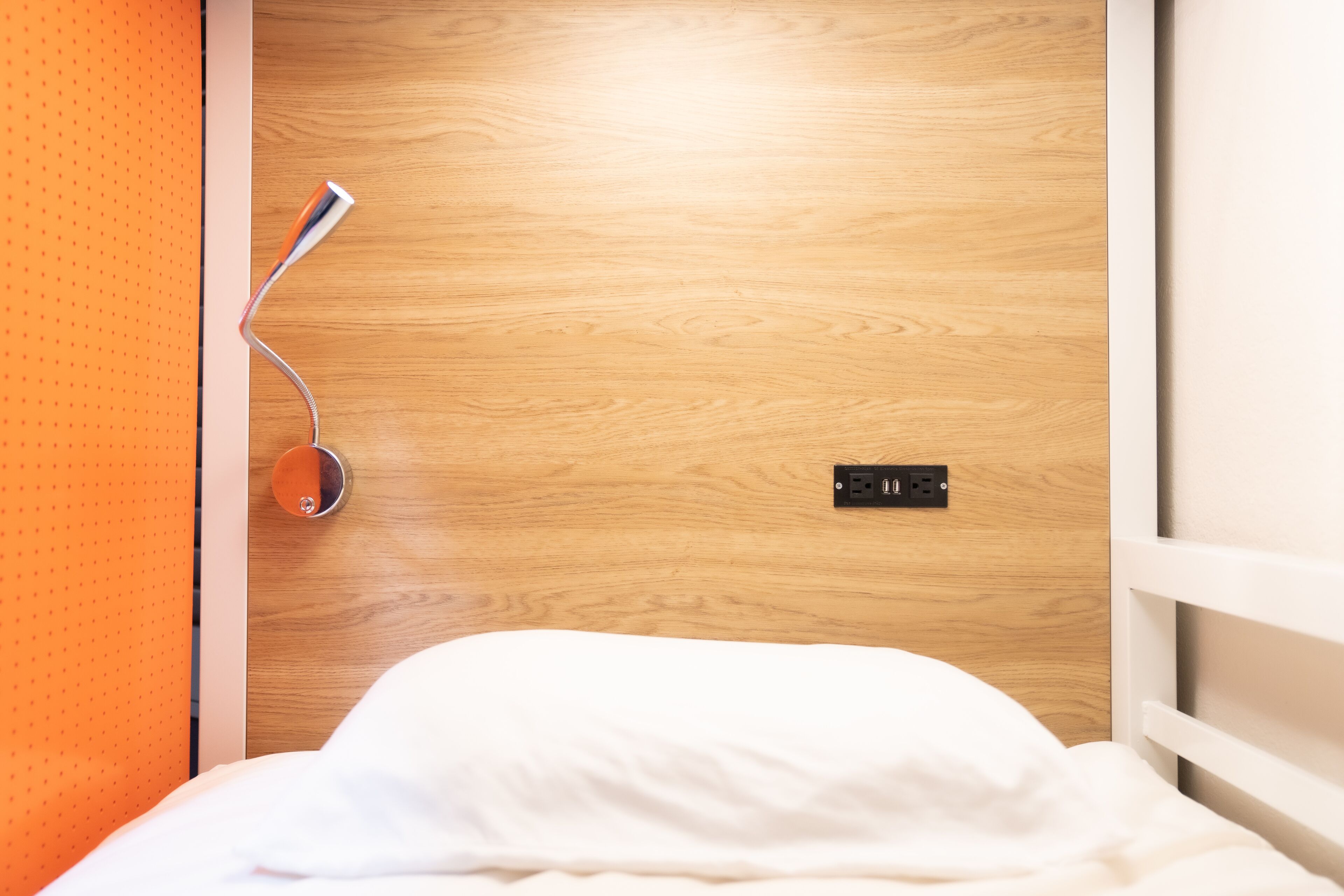 Een hotelkamer met een houten deur, een bed met wit beddengoed en een oranje wand.