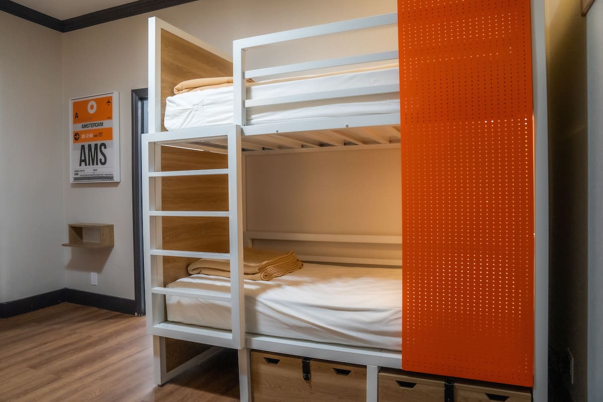 A bunk bed with a wooden shelf and a small shelf unit on the wall.