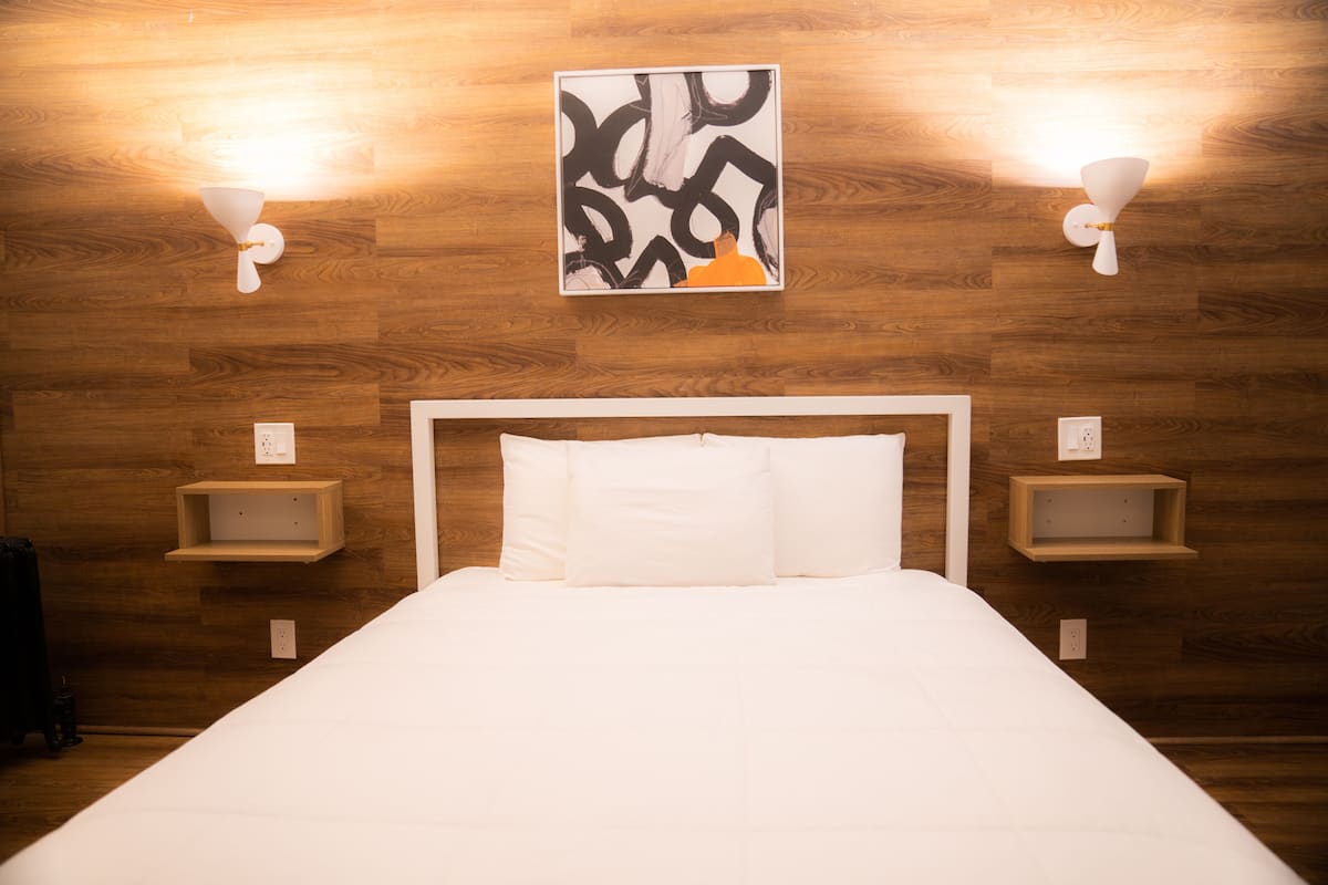 A neatly made bed with white linens in a room with wooden walls and two wall-mounted light fixtures.