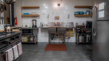 A modern kitchen with stainless steel appliances, a microwave, and a stove. There are wooden shelves above the counter and a red mat on the floor.