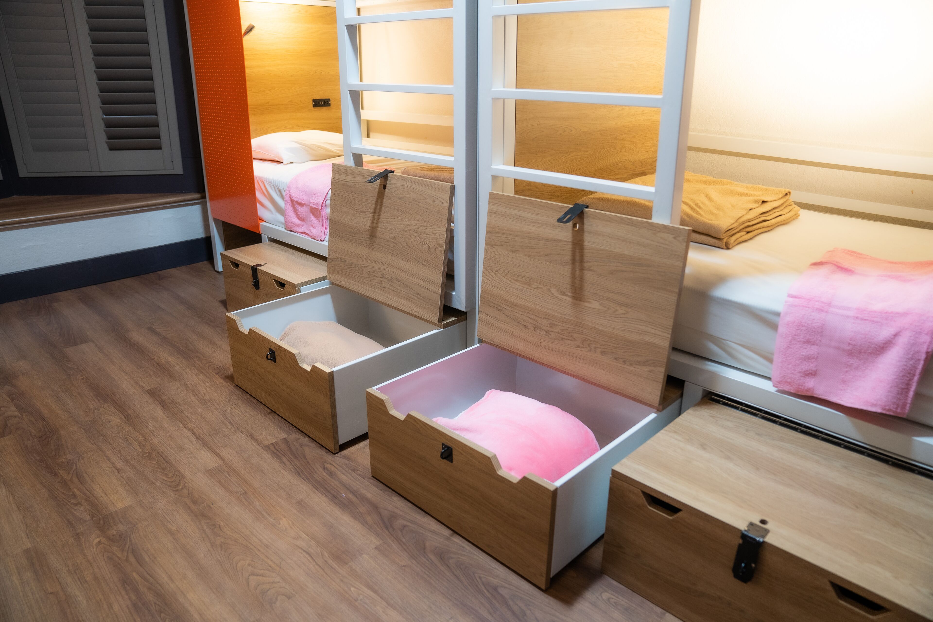 A hotel room with a bunk bed, a wooden floor, and built-in storage drawers.