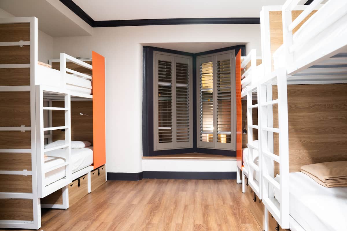 A room with bunk beds, a window with shutters, and wooden flooring.
