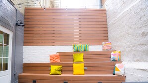 A wooden bench with colorful cushions against a white wall. - Amsterdam Hostel (San Francisco)