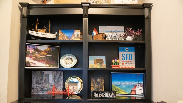 A display cabinet with various travel memorabilia, including a model ship, postcards, and a sign for San Francisco. - Amsterdam Hostel (San Francisco)