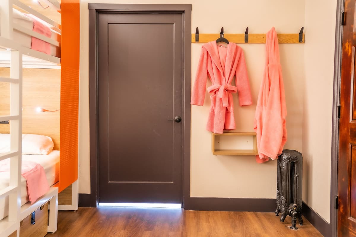 A hotel room with a wooden bunk bed, a dark door, and a wall-mounted towel rack with pink towels.