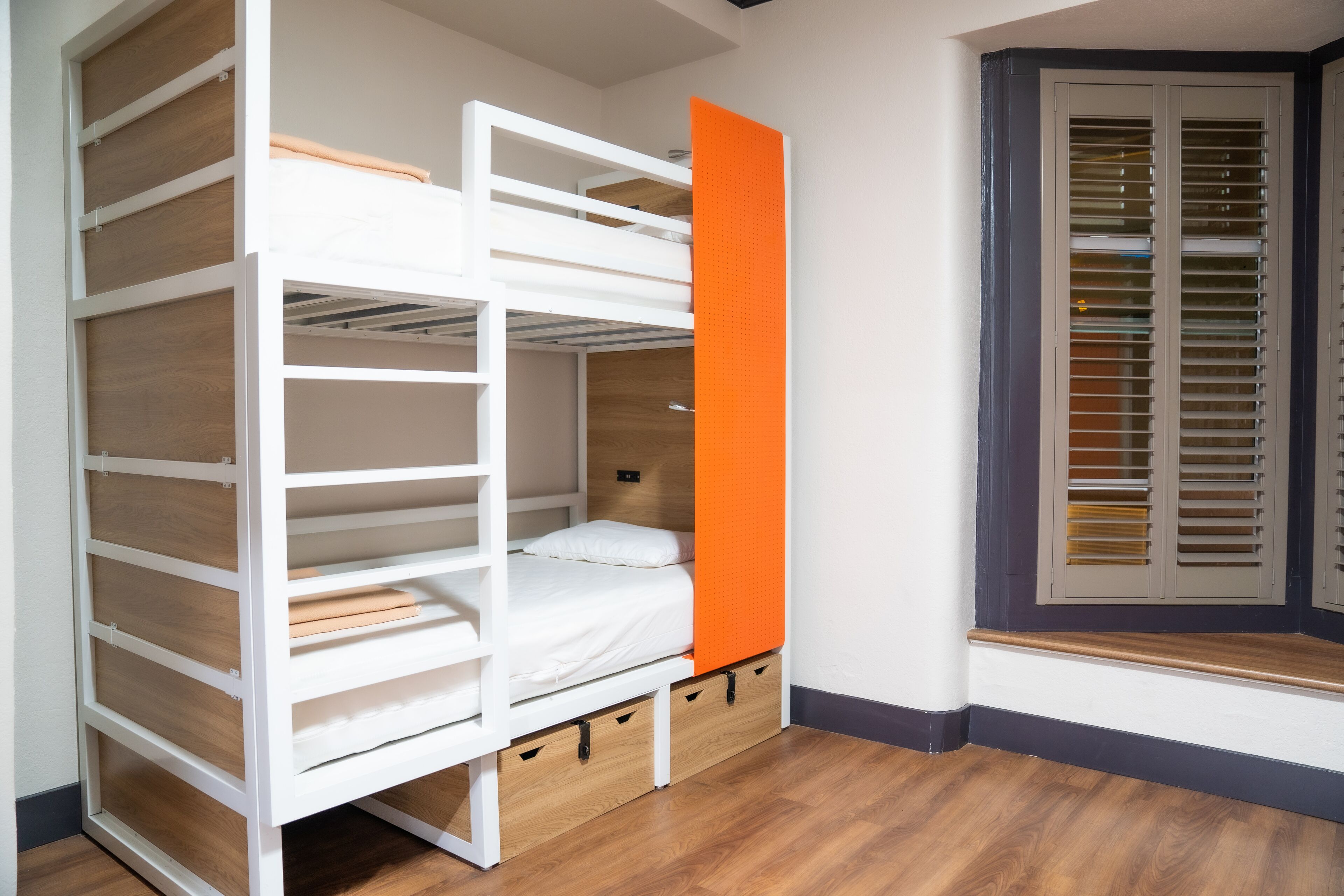 Una cama litera con cajones para guardar objetos, una ventana con contraventanas y suelo de madera.