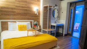 A hotel room with a bed, a bedside table, a mirror, a hanging coat rack, a bathroom with a sink and toilet, and a view of the outside. - Amsterdam Hostel (San Francisco)