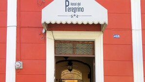Η είσοδος του ξενοδοχείου «Hotel del Peregrino» διακρίνεται από την κόκκινη πρόσοψή του, την λευκή τέντα με την επωνυμία του ξενοδοχείου και την πινακίδα με τον αριθμό της διεύθυνσης.