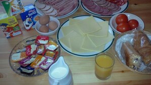 Ein Tisch mit verschiedenen Speisen, darunter Eier, Käse, Schinken, Würstchen, Tomaten, Brot und Beilagen.