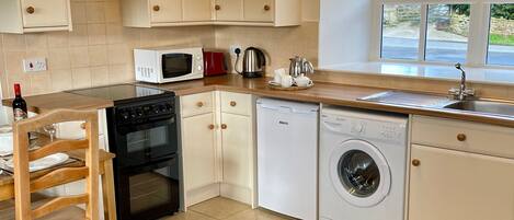Een kleine keuken met een kookplaat, magnetron, spoelbak en wasmachine.