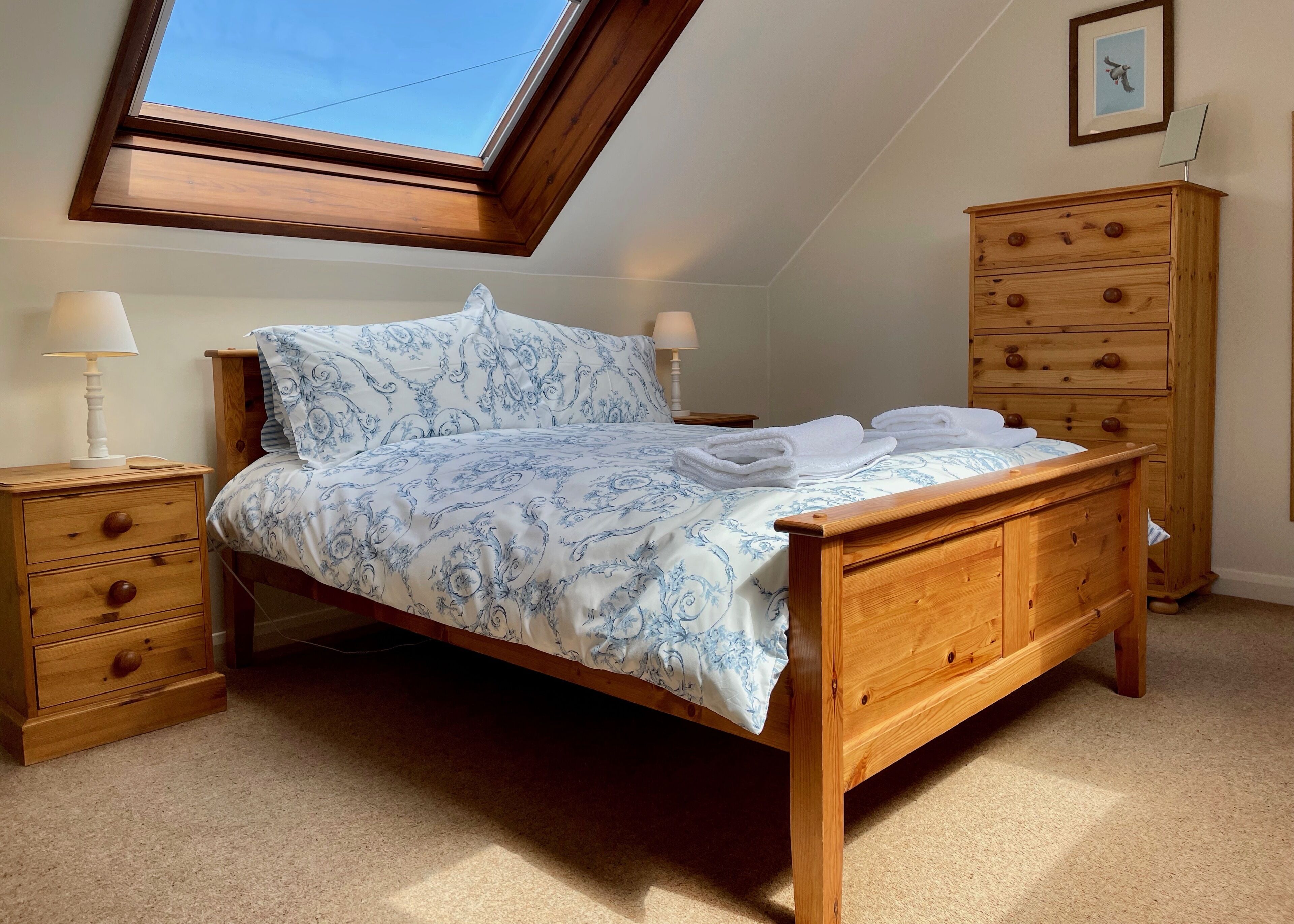 Une chambre avec un puits de lumière, un lit recouvert d’une couvre-lit à motifs, deux tables de chevet avec des lampes et une commode en bois.