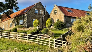 Une maison en pierre avec un toit recouvert de tuiles rouges, une clôture en bois et un jardin bien entretenu.