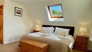 Un lit bien fait, avec une tête de lit, une table de chevet avec une lampe, une commode en bois et une lucarne au-dessus du lit.