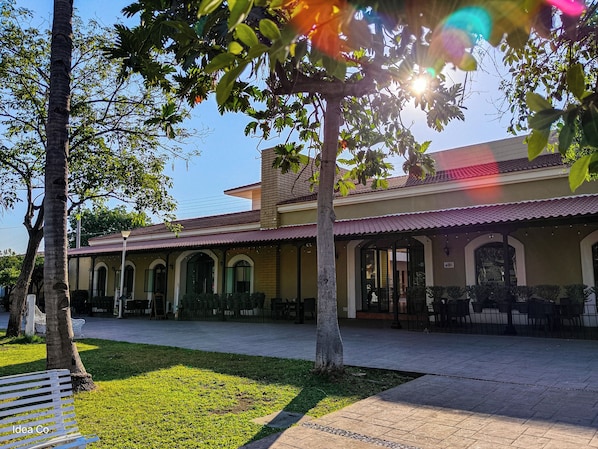 A courtyard with a building featuring arched doorways and a tiled roof. - Concierge Plaza la Villa (Villa de Alvarez)